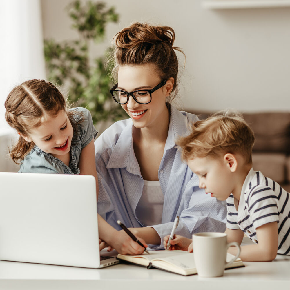 Little children distracting dedicated young woman working on laptop at home
